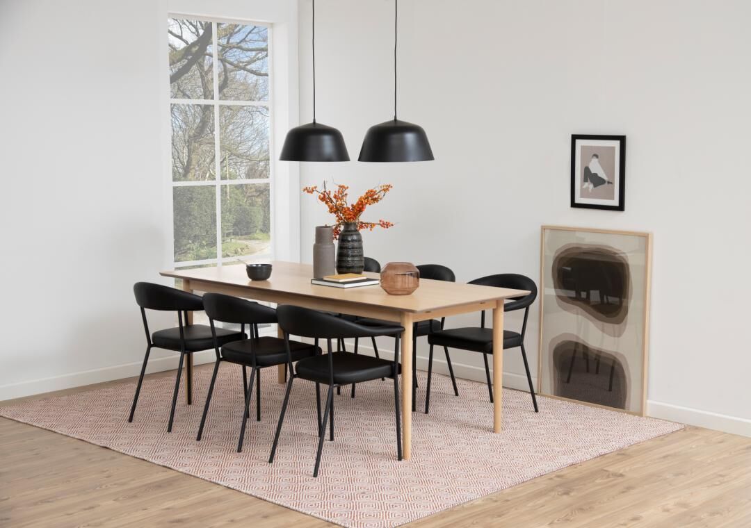 Eetkamer met houten tafel, zwarte Ava eetkamerstoelen met armleuning, hanglampen en kunst aan de muur.