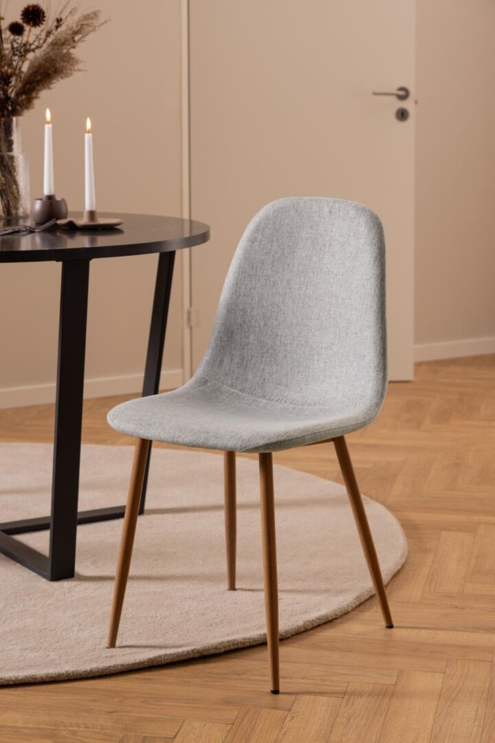 Celia eetkamerstoel: grijze stoel met houten poten naast een ronde tafel.