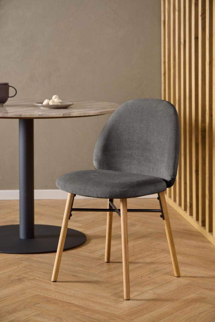 Sophia eetkamerstoel: grijze stoffen stoel met houten poten bij een ronde tafel.