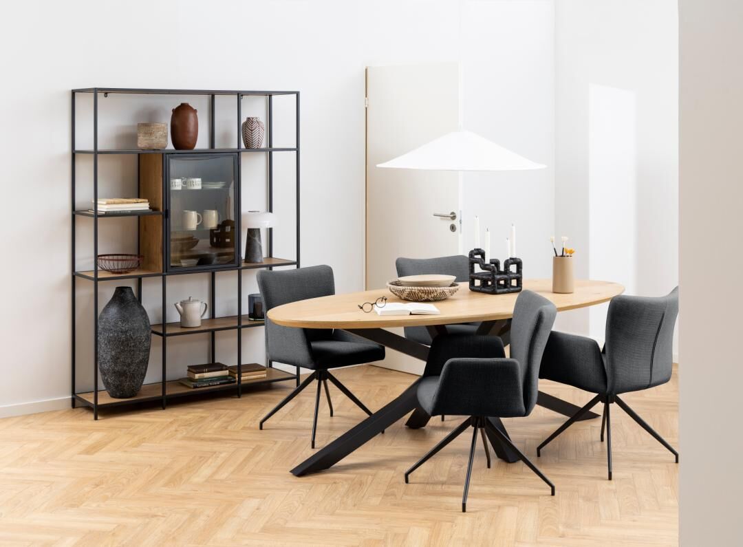 Eetkamer met ovale houten tafel, grijze Laura eetkamerstoelen met armleuning en zwart metalen stellingkast.