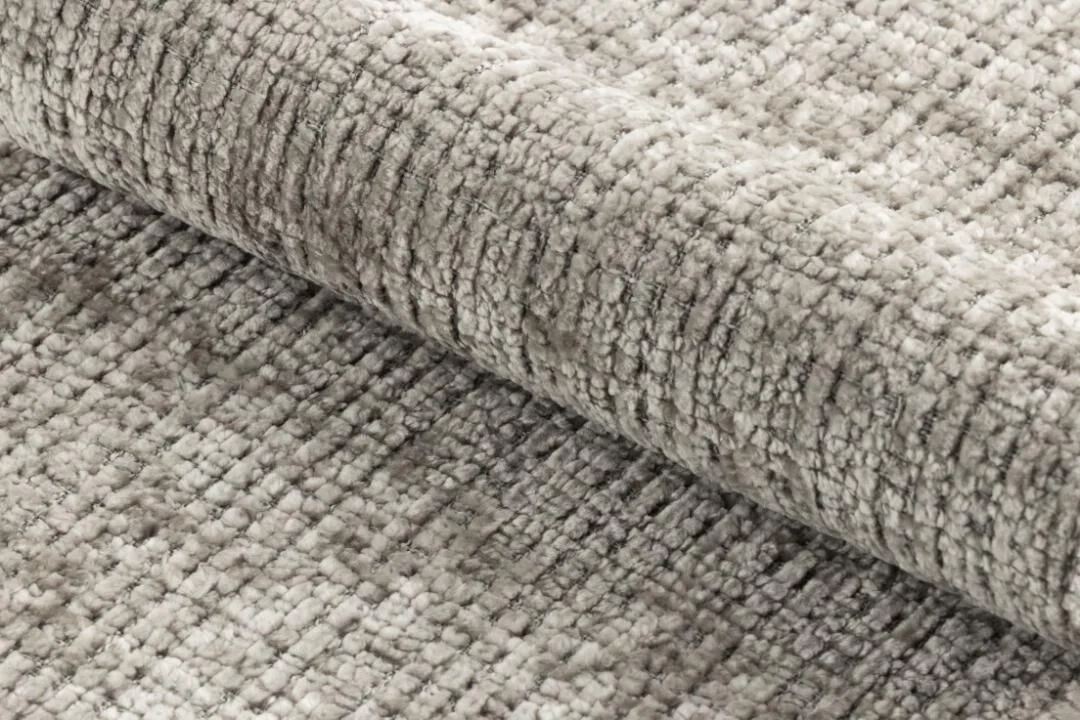 Grijze, getextureerde vloerkleed, opgerold, met subtiele details.