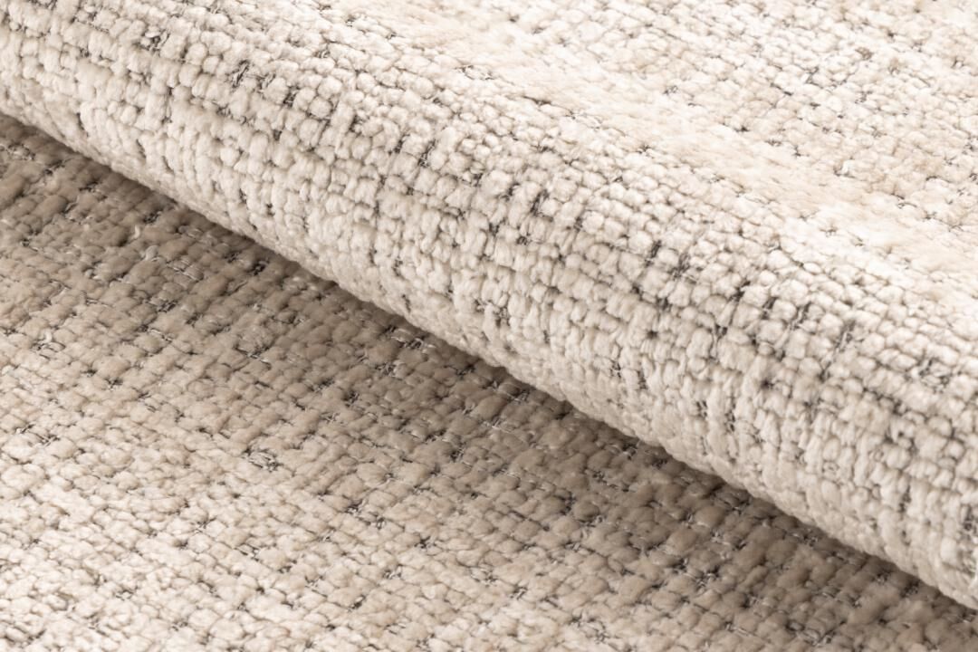 Beige vloerkleed met subtiel geometrisch patroon, opgerold detail.