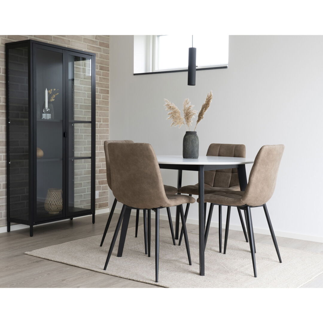Middelfart eetkamerstoelen in lichtbruin microvezel met zwarte poten aan een ronde eettafel, naast een zwarte vitrinekast.