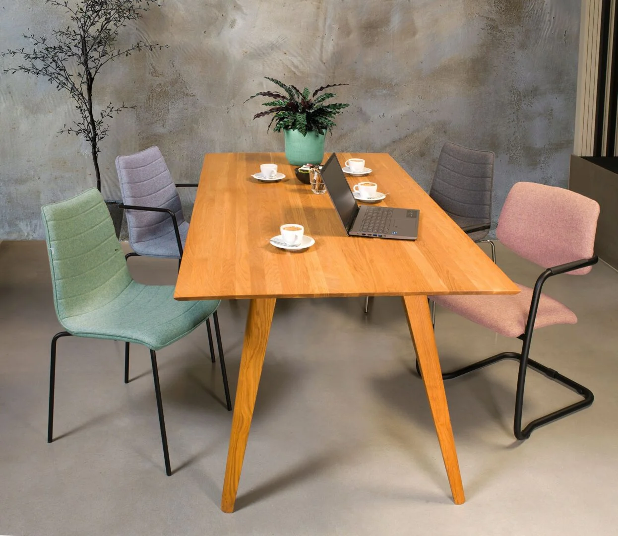 Houten eettafel met vier stoelen, laptop, koffiekopjes en plant. Workliving Verona Armstoel Roze Wolvilt | Nieuwe Sfeer