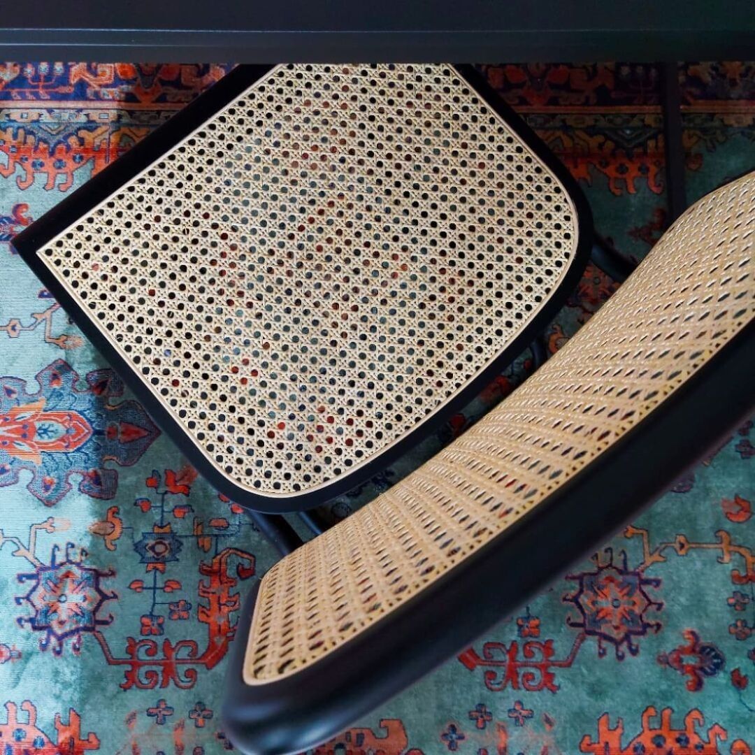 Set van 4 rotan eetkamerstoelen met zwart onderstel op een kleurrijk vloerkleed.