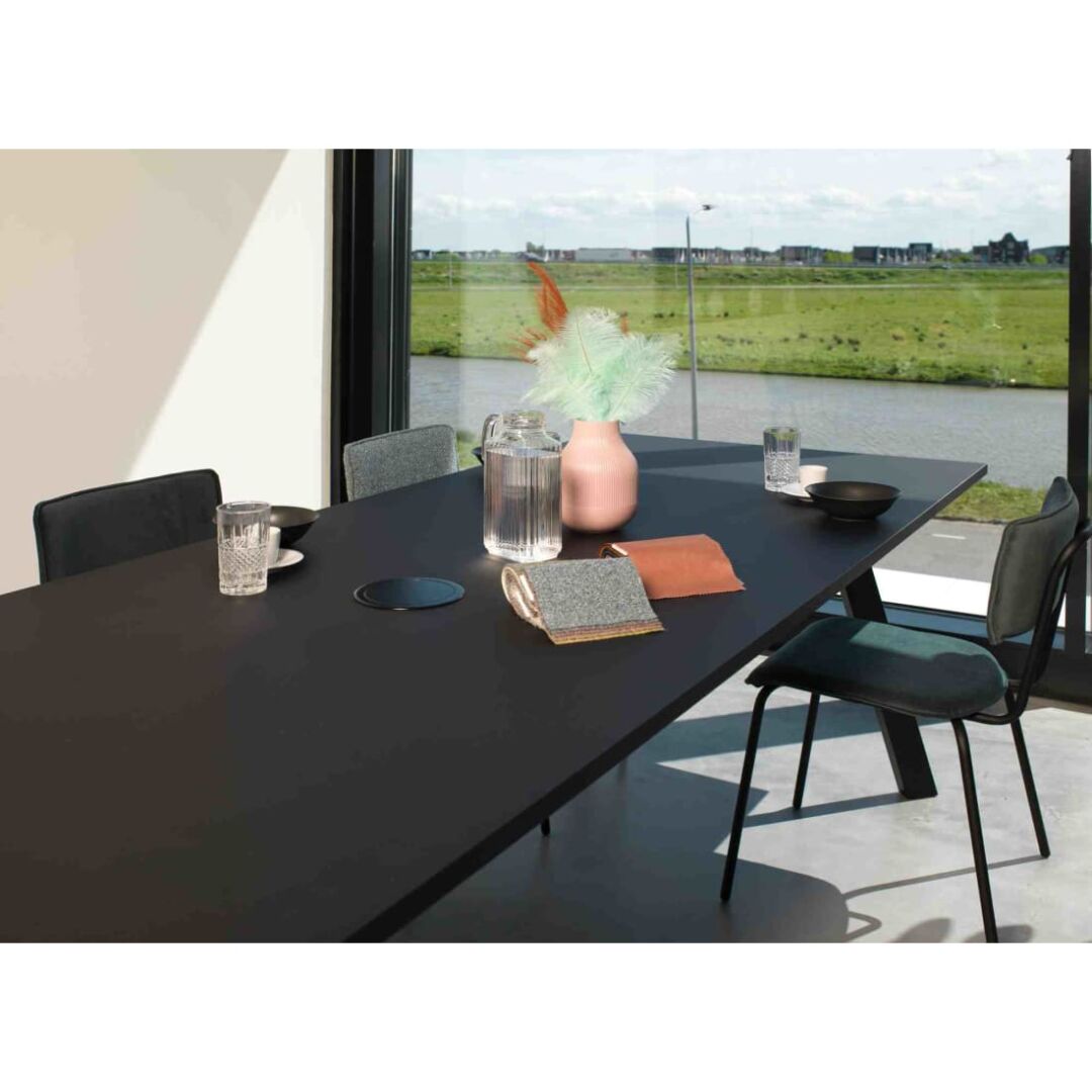 Workliving Bo Society Eetkamerstoel Bouclé Mosterd aan zwarte eettafel met uitzicht op groen landschap.