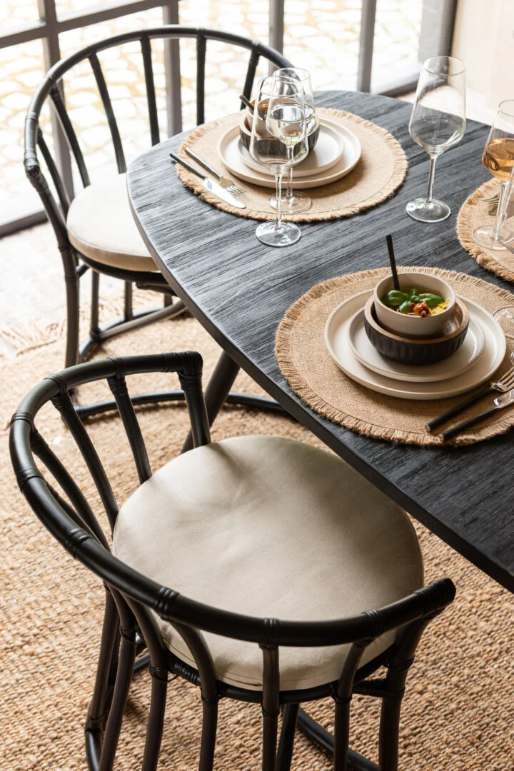 Eetkamerstoel Rotan Zwart met Wit Kussen van Nieuwe Sfeer aan een eettafel.