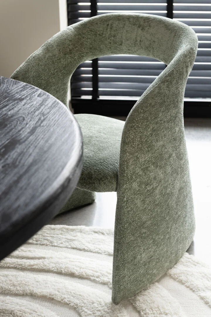 Stoel Anise Stof Beige van Nieuwe Sfeer: groene design stoel met gebogen rugleuning naast een donkere houten tafel.