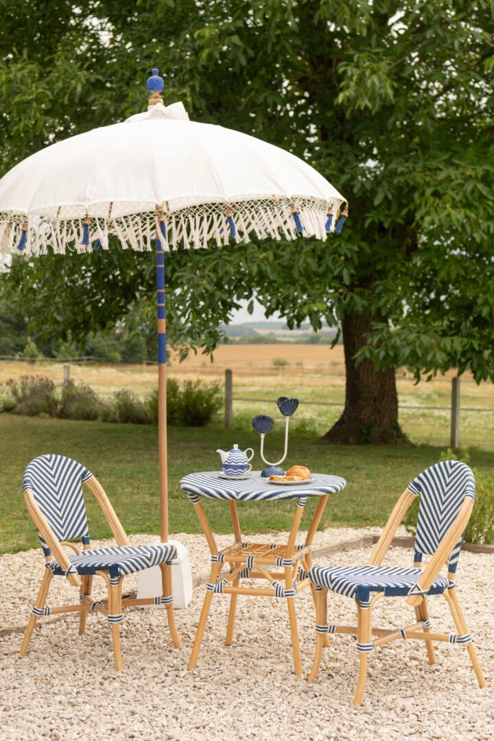Eetkamerstoel Geo Rotan Blauw Wit: Bistroset met blauw-wit gestreepte stoelen en parasol voor buiten.
