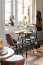 Stoel Loft Leer Metaal Zwart van Nieuwe Sfeer: bruine en zwarte leren stoelen aan een ronde tafel bij een raam.