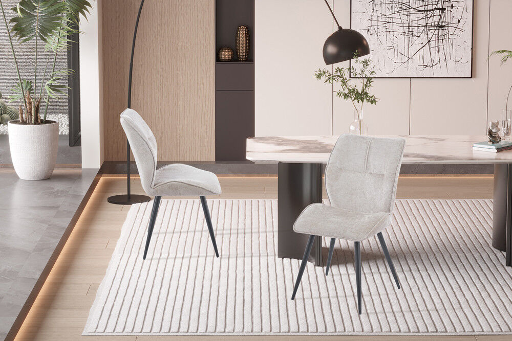 Eetkamerstoel Faye Zand Stof: beige stoffen stoelen met zwarte poten op een lichte vloerkleed.