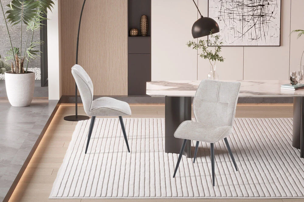 Eetkamerstoel Faye Zand Stof: beige stoffen stoelen met zwarte poten op een lichte vloerkleed.