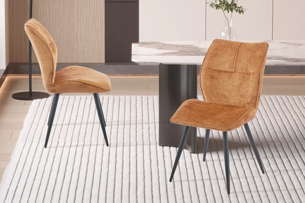 Eetkamerstoel Faye Goud Stof op een gestreepte vloerkleed. Twee stoelen worden getoond.