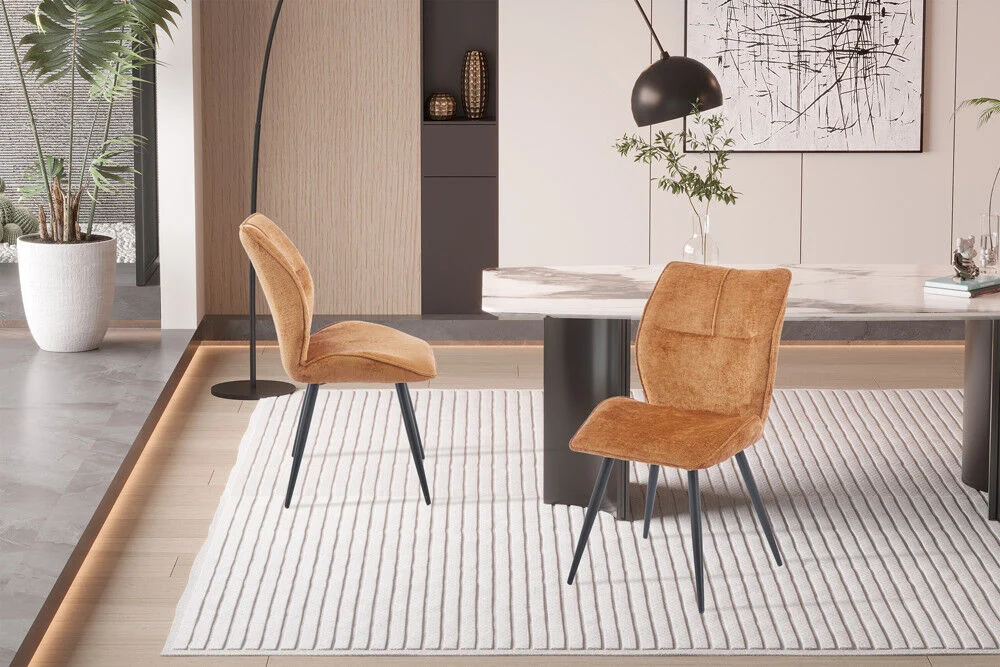 Eetkamerstoel Faye Goud Stof: Gouden velvet eetkamerstoelen met zwarte poten op een wit vloerkleed.
