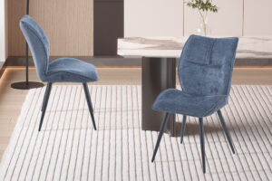 Eetkamerstoel Faye Blauw Stof: Blauwe stoffen eetkamerstoel met zwarte metalen poten op een gestreepte vloerkleed.