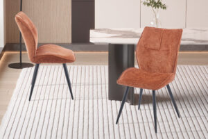 Eetkamerstoel Faye Roest Stof: Twee roestkleurige stoffen eetkamerstoelen met zwarte metalen poten op een gestreept vloerkleed.