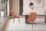 Eetkamerstoel Faye Roest Stof: Twee roestkleurige, gestoffeerde stoelen op een gestreepte vloerkleed in een moderne eetkamer.