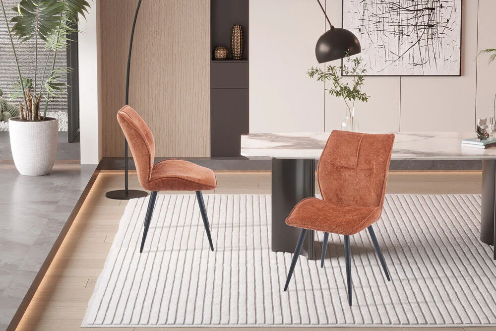 Eetkamerstoel Faye Roest Stof: Twee roestkleurige, gestoffeerde stoelen op een gestreepte vloerkleed in een moderne eetkamer.