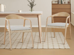 Eetkamerstoel Claire Essenhout Naturel Beige: Twee houten stoelen met beige kussens bij een tafel.