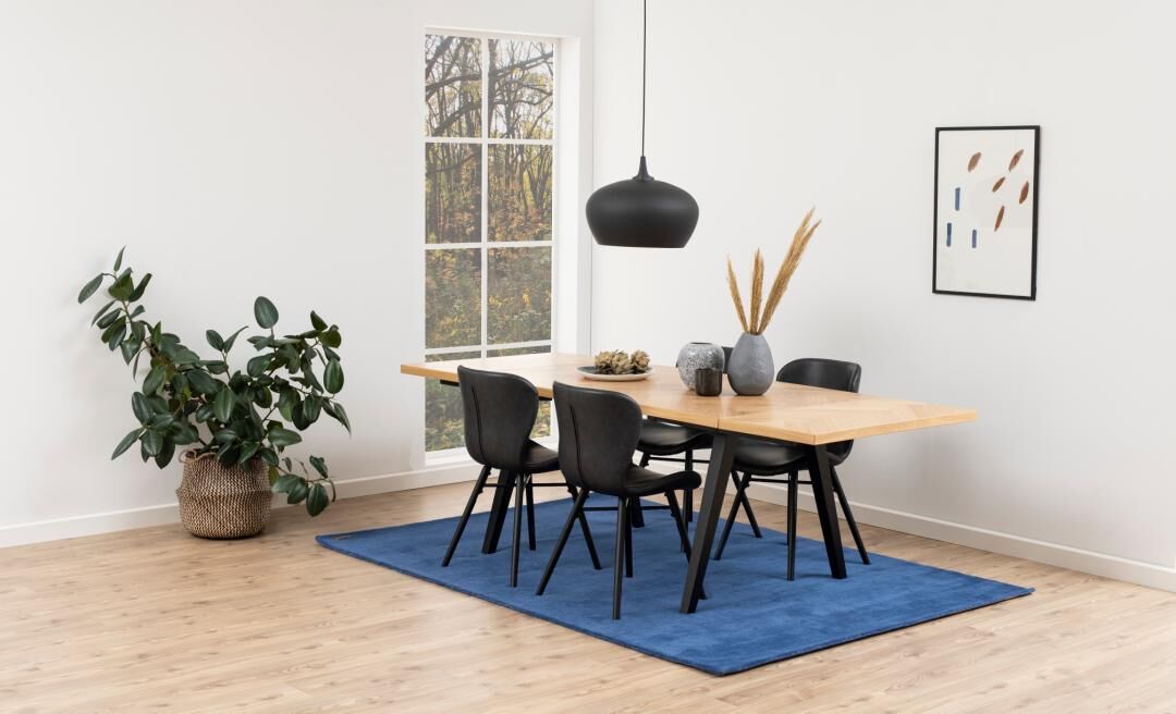 Eetkamer met Batilda -A1 eetkamerstoelen (set van 2), houten tafel, blauw vloerkleed, plant en kunst aan de muur.