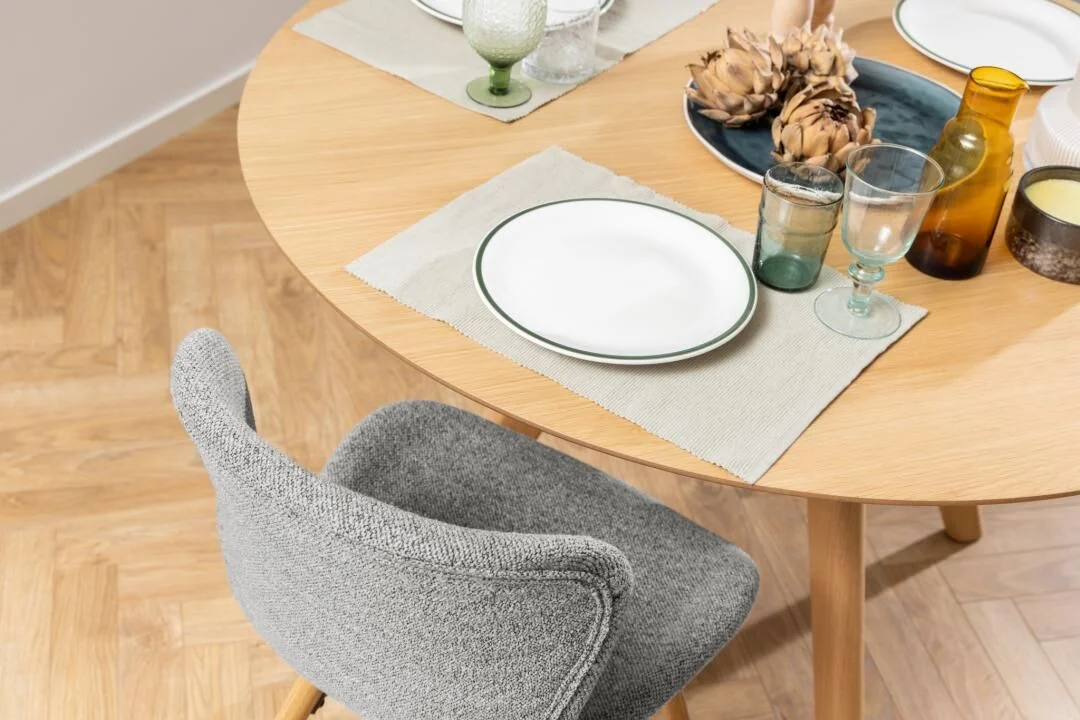 Batilda -A1 eetkamerstoel: Grijze gestoffeerde stoel aan ronde houten eettafel.