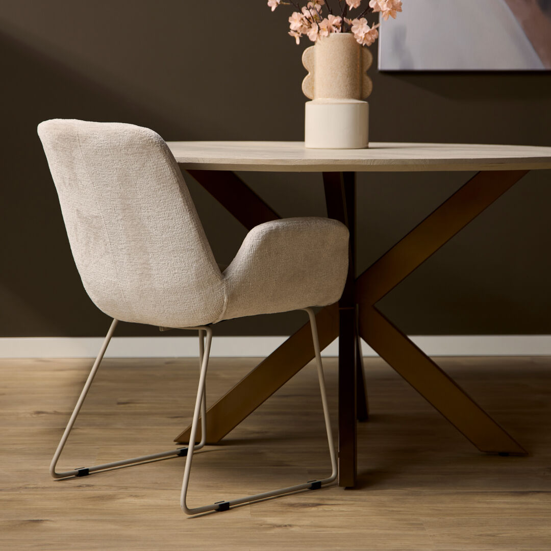 Eetkamerstoel Evan Zand | Nieuwe Sfeer: Beige gestoffeerde stoel met metalen frame bij een ronde houten tafel.