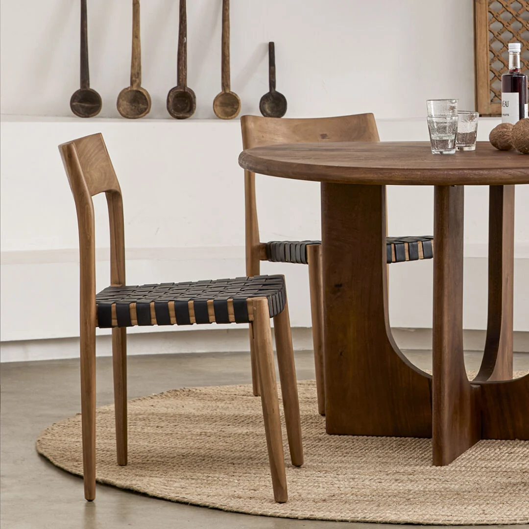 Freya teak eetkamerstoel met leer - Zwart (set van 2) bij een houten tafel op een jute vloerkleed.