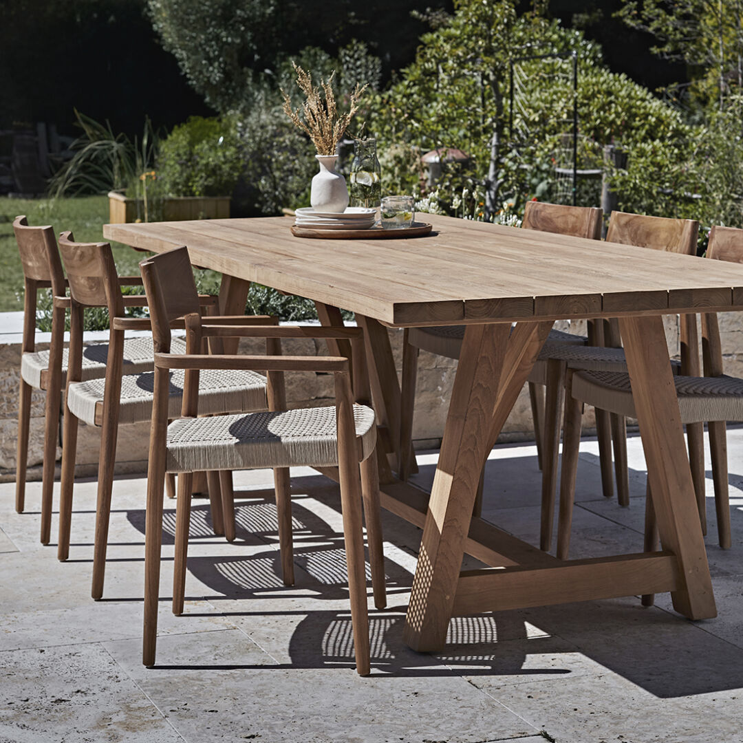 Freya donker teakhouten tuinstoel met armleuning - naturel (set van 2) bij een houten tuintafel.