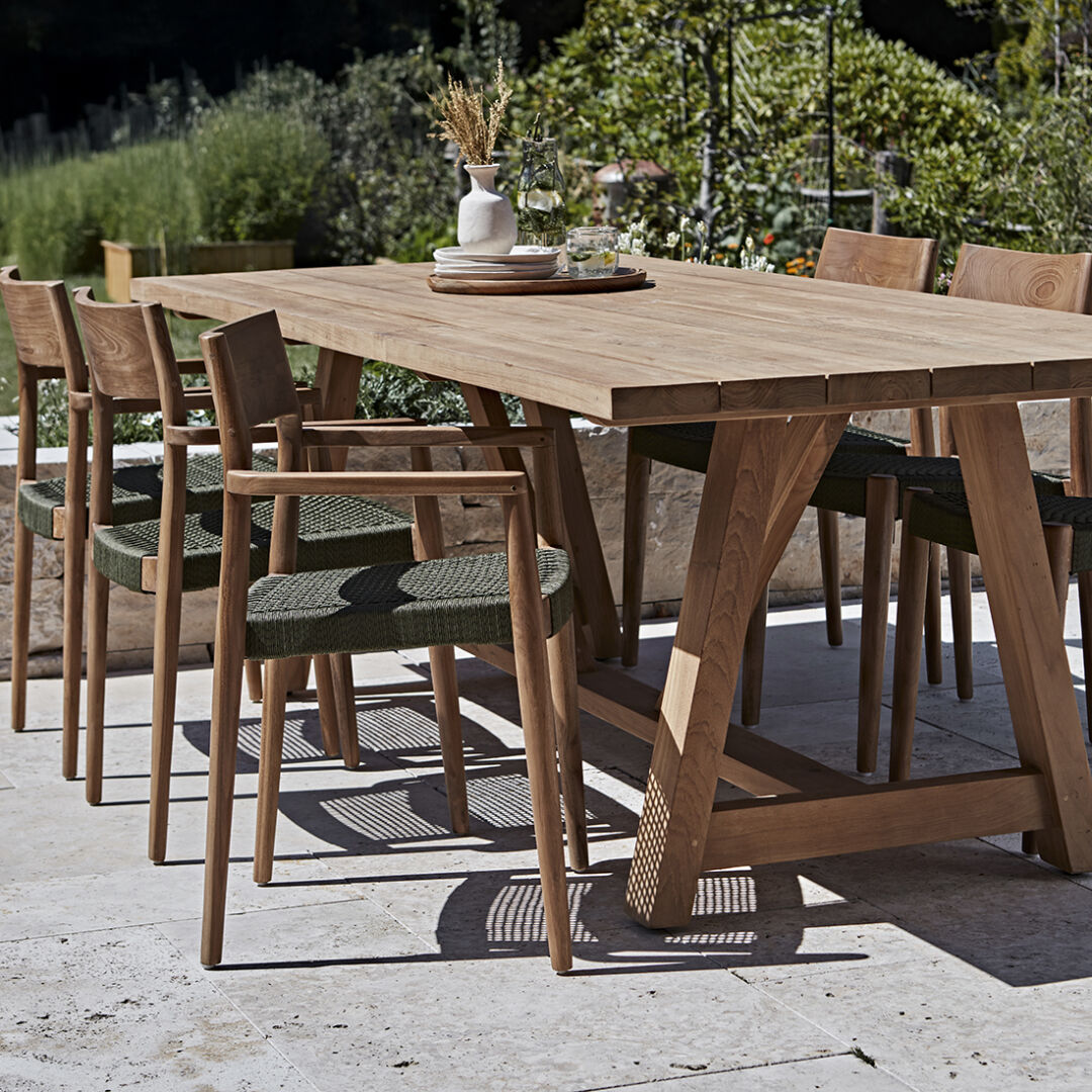 Freya donker teakhouten tuinstoel met armleuning - groen (set van 2) bij een houten tuintafel.