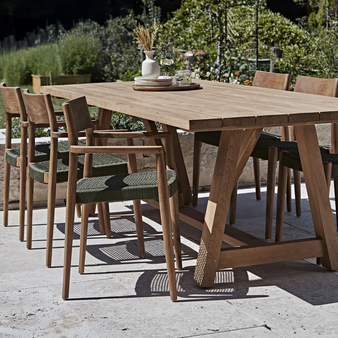 Freya donker teakhouten tuinstoel met armleuning - groen (set van 2) bij een houten tuintafel.