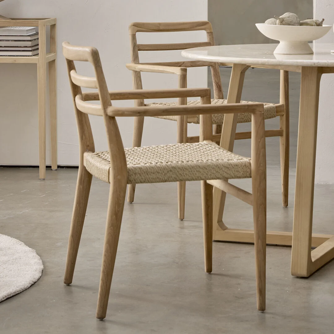 Verano teak tuinstoel naturel met armleuning, set van 2, naast een ronde tafel.