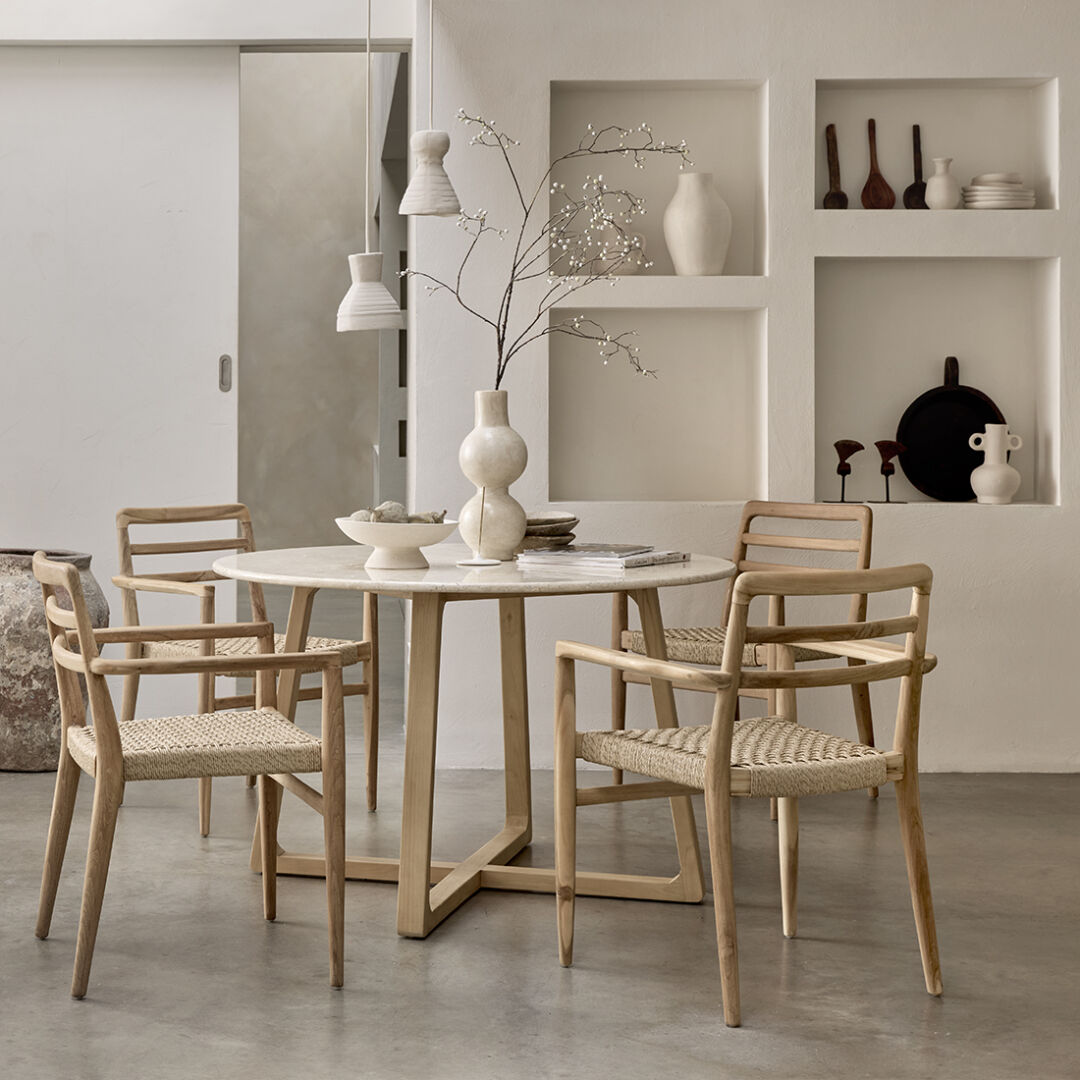 Verano teak tuinstoel met armleuning naturel bij een ronde eettafel in een lichte ruimte.