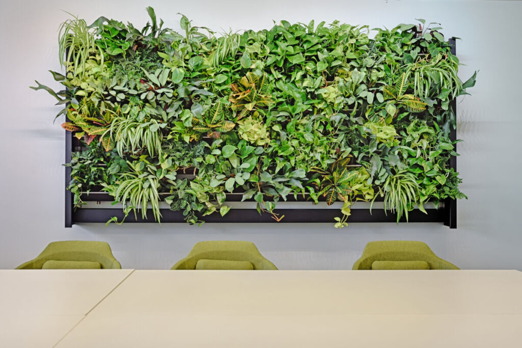 Groene plantenwand boven tafel en stoelen in een kantoorruimte.