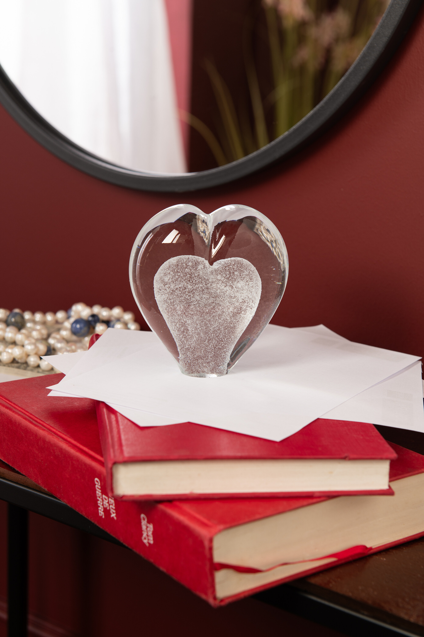 Brirnesta wit glazen presse-papier in hartvorm op papieren en rode boeken, compact en decoratief