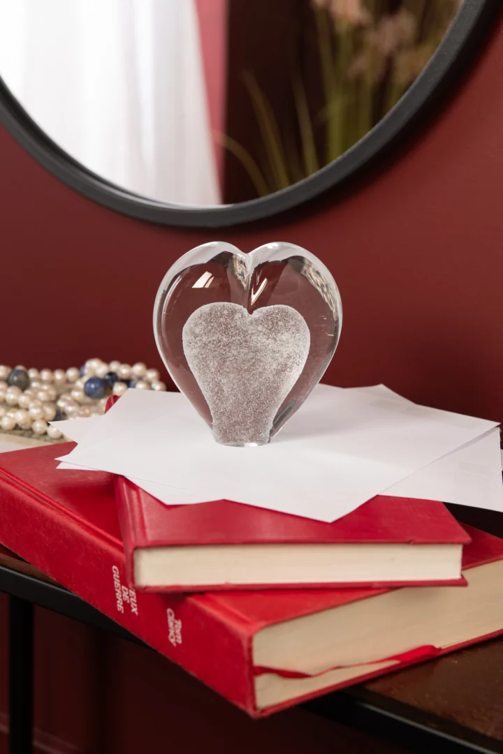 Brirnesta wit glazen presse-papier in hartvorm op papieren en rode boeken, compact en decoratief