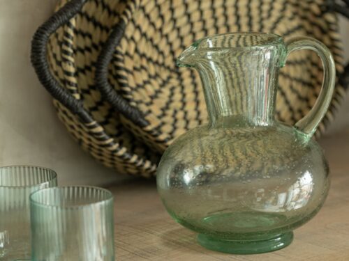 Drinkglas Daltira Glas Groen met geribbelde afwerking op een houten tafel, naast een groen glazen karaf