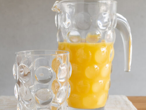 Transparant Limonadeglas Ciessino van glas met reliëf, naast karaf met sinaasappelsap op gedekte tafel
