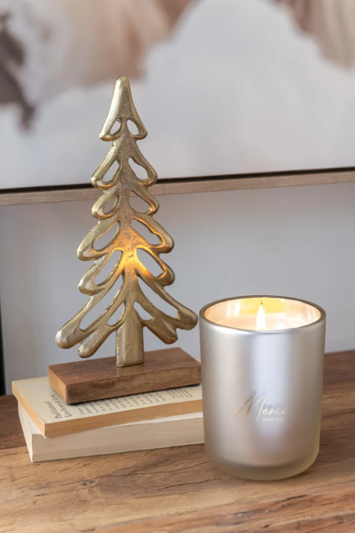 Geurkaars Zeirmello Palmwas Beige in matglas, brandend naast gouden kerstboomdecoratie op boeken
