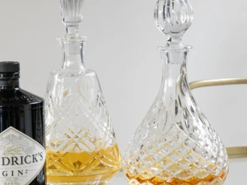 Karaf Sleermona glas transparant met slanke vorm en geslepen details, gevuld met amberkleurige drank