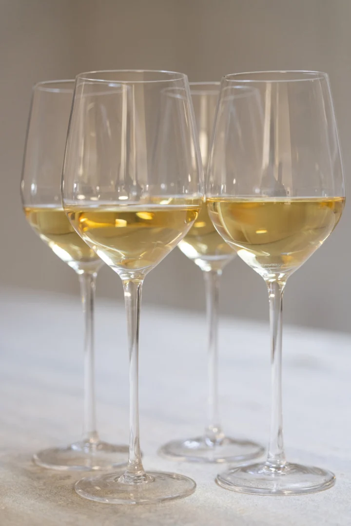 Transparant Gooskino drinkglas met slanke vorm en lange steel, gevuld met witte wijn in een elegante setting