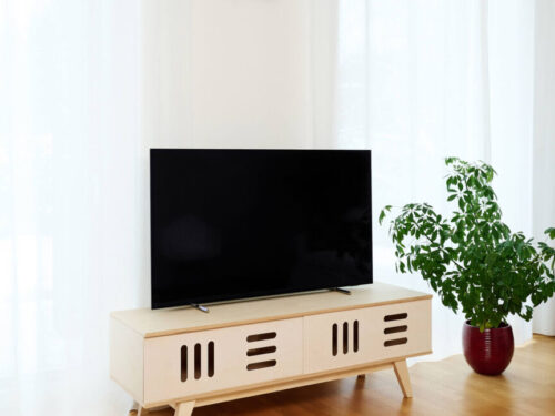 TV-meubel Permar 150 cm in naturel hout met witte schuifdeuren onder een grote tv in een lichte woonkamer