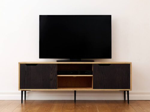 TV-meubel Ziske 150 cm met eikenfineer, zwarte deuren en slanke metalen poten onder een tv