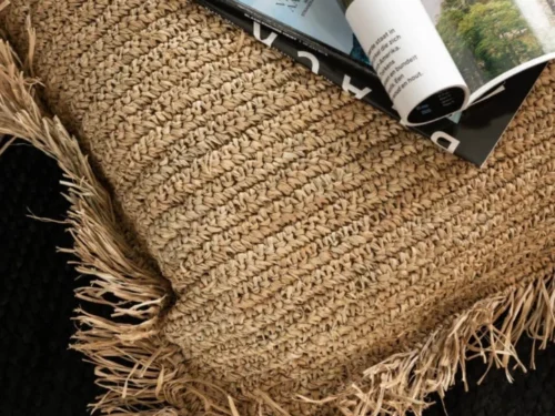 Kussen Floodano Naturel 45x45 cm met geweven raffia look en speelse franjes op een zwarte bank