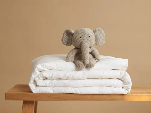 Dekbedovertrek Grurnol Wit opgevouwen, met zachte satijnglans en teddy olifant op een houten tafel