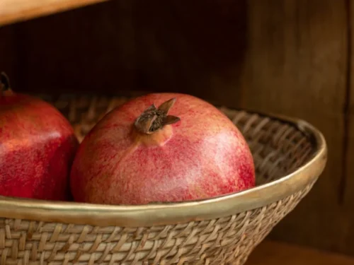 Rotanmand Tampere Rotan Goud met messing rand, gevuld met granaatappels in houten kast