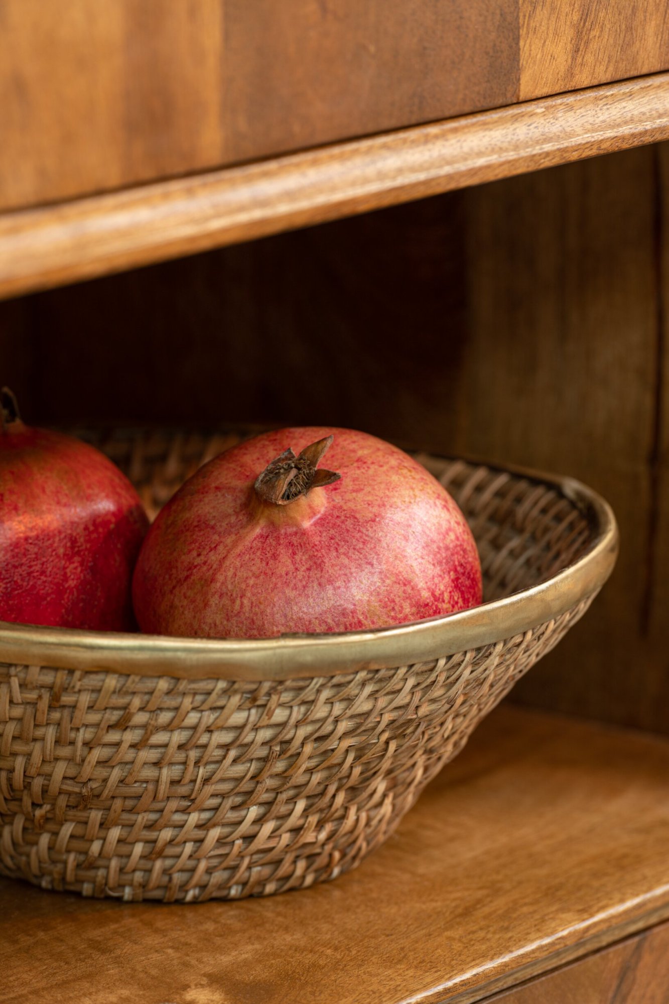 Rotanmand Tampere Rotan Goud met messing rand, gevuld met granaatappels in houten kast