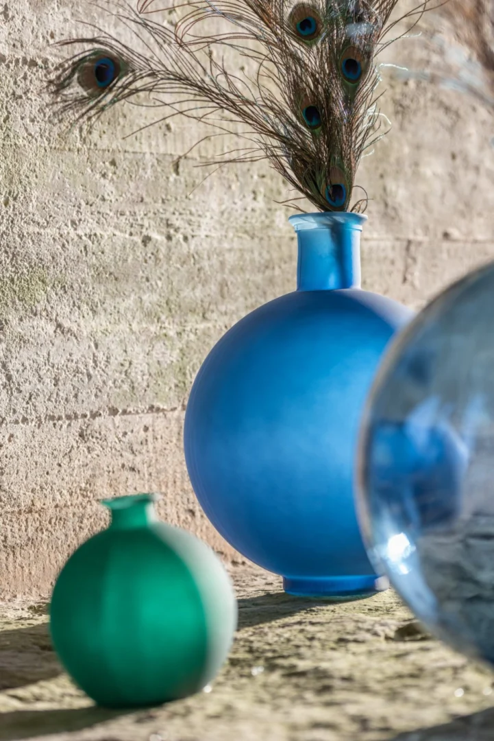 Bolvaas Tisero glas groen, matte ronde vaas met pauwenveren op rustieke stenen ondergrond