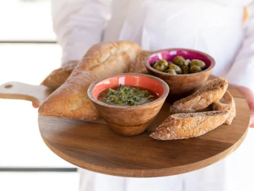 Kom Taanon mangohout, meerkleurig, met warme binnenkant op houten serveerplank met brood en olijven