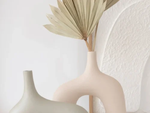 Beige aluminium vaas Leeskil met slanke vorm, gevuld met droog palmblad in een rustige, moderne setting
