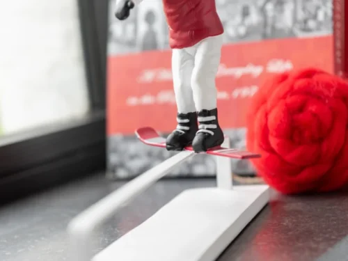 Keskun meerkleurig polyresin woonaccessoire, winters ski-figuurtje in rood en wit op een decoratieve skistandaard